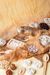 Glass of water, many food supplements in forms of tablets, pills and capsules on beige background in rustic style. Dietary supplements, vitamins and minerals for healthy lifestyle.
