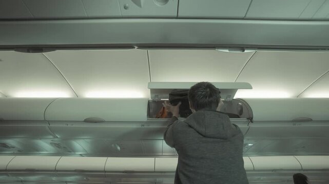 A passenger places their bag in the overhead compartment of an airplane. The photo captures the experience of traveling and navigating the cabin space.