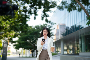 Fototapeta premium Focused businesswoman walking while using smartphone