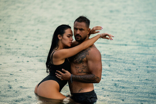 Attractive couple in passionate embrace in water. Beautiful young woman and her sexy boyfriend touching each other on the beach. Fashion models. Summer vacation on the beach. Erotic couple.
