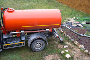The orange tank of the sewage disposal machine in the courtyard of the house sucks sewage waste...