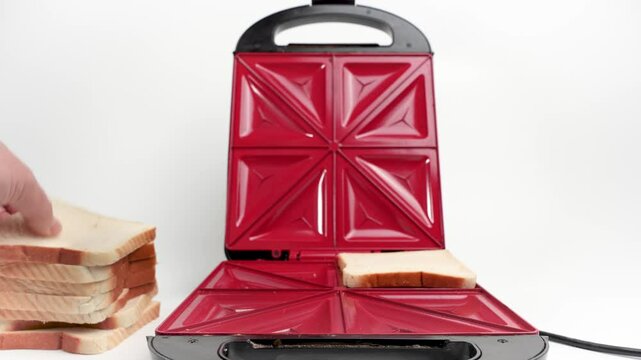 Puts bread into an electric sandwich maker to make sandwiches. Electric sandwich maker on white background.