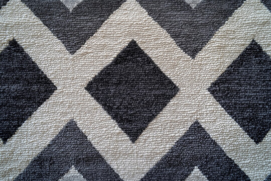Dark gray and white chevron pattern carpet, textured background. Flat lay. Top view of gray and beige geometric textile fabric with triangular shapes for interior design in a home