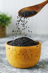 black sesame seeds falling from spoon in bowl on table
