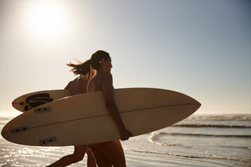 Couple, sunset and walking with surfboard on beach for swim, surf or extreme sport together in...