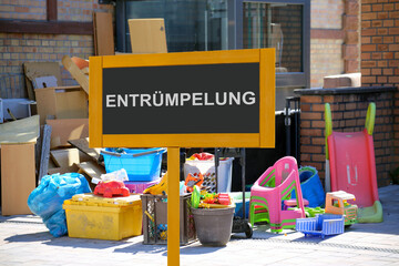 (Fotomontage) Schild mit der Aufschrift ENTRÜMPELUNG vor Sperrmüll an einem Wohnhaus