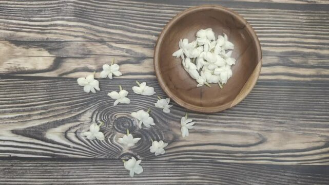 A bunch of White Jasmine or Jasminum sambac flowers in a small wooden bowl on a wooden table.