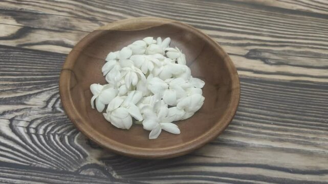 A bunch of White Jasmine or Jasminum sambac flowers in a small wooden bowl on a wooden table.
