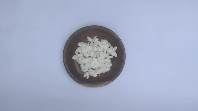 A bunch of White Jasmine or Jasminum sambac flowers in a small wooden bowl on a white background