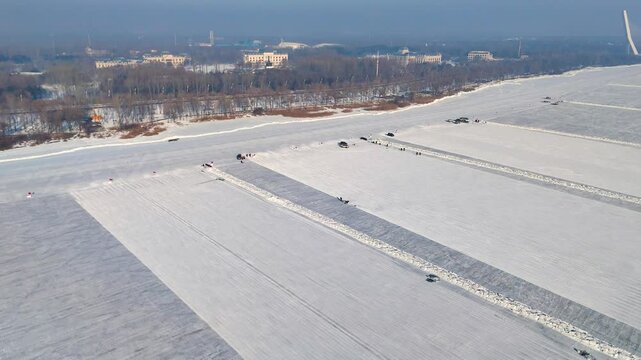 Aerial view of ice-cutting machines at work on the frozen Songhua River in Harbin, creating parallel cuts in the ice. The vast, snow-covered surface is prepared for the ice blocks. China