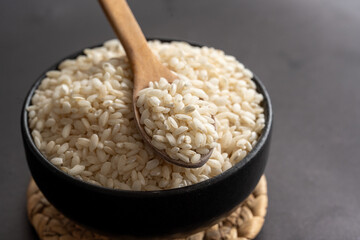 Macro photography of white short grain rice in wooden spoon on dark background. Short white rice in wooden spoon. Closeup photo of rice. 