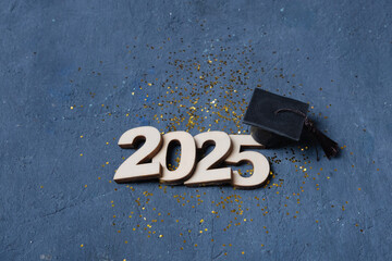 Graduation cap on wooden number 2025 on dark background. Class of 2025 concept