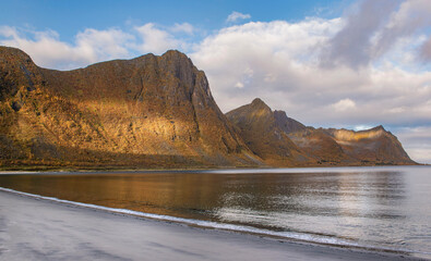 view from the beach on  large mountains  in a fjork at Skaland in the Senja island in Norway. illuminated by the sun