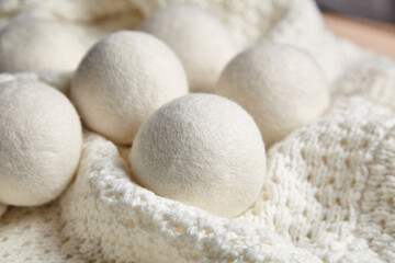 White wool dryer balls placed on a textured knitted blanket, creating a cozy, eco-friendly aesthetic. Emphasizes natural and sustainable laundry care in a warm setting.