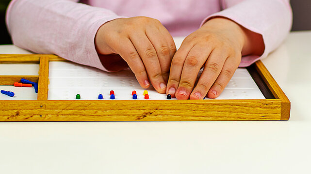 A blind girl uses a Braille learning board to explore the alphabet through touch. Her delicate fingers carefully press the tactile markings, emphasizing the importance of sensory learning for visually