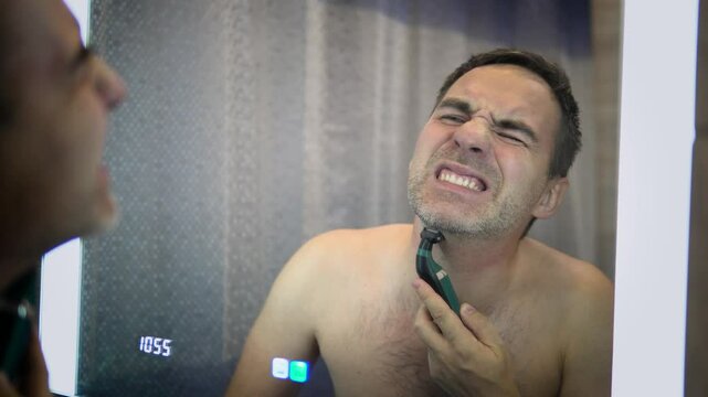 Young bearded man during grooming of beard using trimmer. Half face with a beard half shaved. shaving with a razor blade. man experiences pain and suffering while shaving.