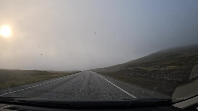 Driving on the E69 road through the tundra in northern Norway. Misty hills covered with grass and scattered stones surround the route, creating a remote and atmospheric landscape.