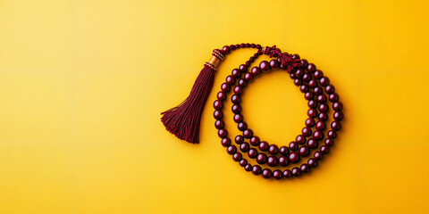 Tibetan prayer bead necklace (mala) with ornate tassel, elegantly coiled on a bold yellow background