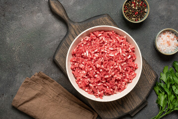 Raw mince beef with spices, ground meat in bowl on wooden cutting board, dark grunge background, top view, flat lay