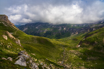 Fototapeta premium The Grossglockner mountain range in Austria with a winding road leading to the lake.The road is surrounded by lush green grass.