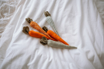 Handmade fabric carrots arranged on a soft white blanket in a cozy setting
