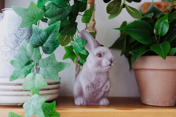 Decorative rabbit figurine among greenery on a wooden shelf