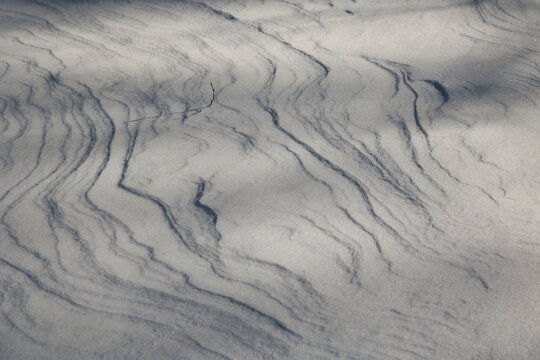 dettagli della superficie di un terreno naturale coperto dalla neve con forme variabili disegnate dal vento ed illuminate dal sole, di giorno, in inverno