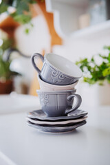 Stacked gray cups and saucers on a white table with green plants nearby