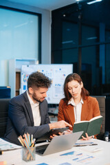 Two office colleagues discuss ideas for a startup project in a modern workspace, using laptops and smartphones