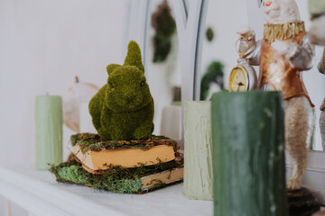 Green moss bunny sits on a stack of vintage books with candles nearby