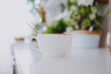 Warm cup of coffee on a bright table with greenery in background
