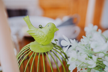 Decorative green bird atop a wire cage with white flowers in a cozy setting