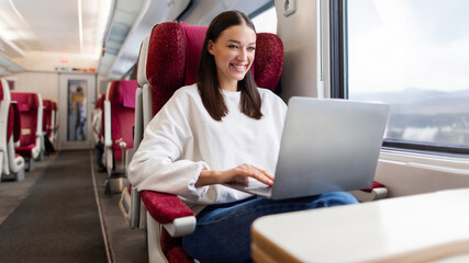 Young European freelancer woman traveling by train, working online with her laptop computer during...