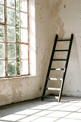 A Striking Interior Scene Featuring a Black Ladder Bathed in Natural Light Through Weathered Windows, Illustrating the Beauty of Minimalist Architecture and Abandoned Spaces