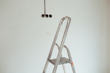 Metal ladder positioned against a plain white wall with light fixtures
