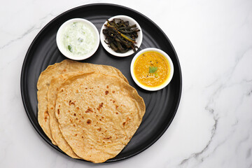 Roti and Sabzi. Indian vegetarian Thali includes bhindi fry, yellow daal tadka, cucumber raita, and chapati or tel paratha. Indian food is served in a plate or thali. Copy Space. healthy Veg Thali