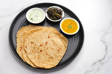 Roti and Sabzi. Indian vegetarian Thali includes bhindi fry, yellow daal tadka, cucumber raita, and chapati or tel paratha. Indian food is served in a plate or thali. Copy Space. healthy Veg Thali