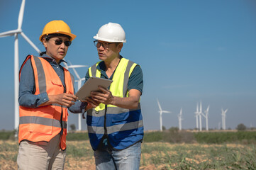 Japanese engineer man working with Asian female wind turbine technician holding laptop in wind energy plant 