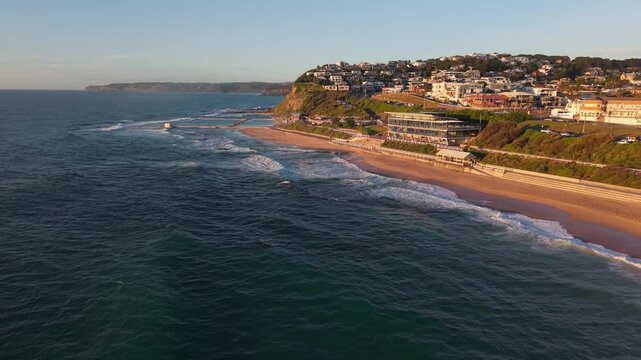 A drone soars along coast from Merewether Surfhouse overlooking the beach and stunning golden sandy shores at sunset