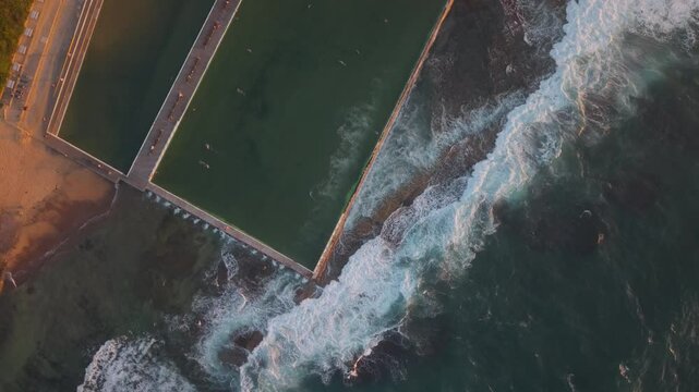 Top down overview aerial of Merewether Ocean Baths with waves crashing along the shoreline, vibrant textures
