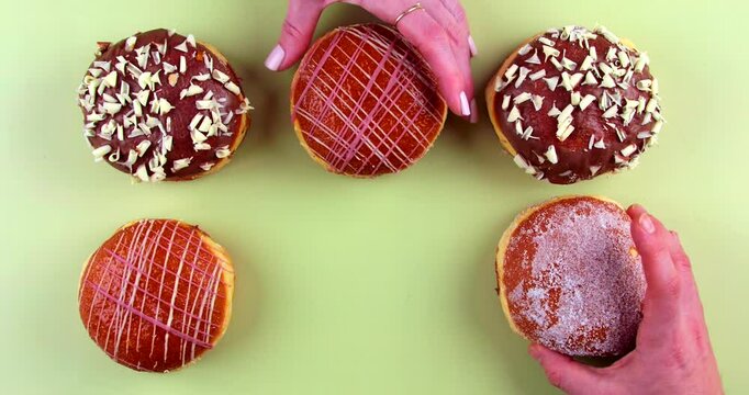 Different hands reaching in to grab Berliner doughnuts one after the other. The assorted donuts are topped with chocolate, almonds, powdered sugar, and icing, arranged on a green background.