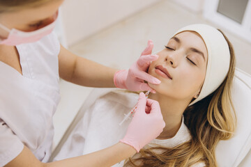 Beautician making injection of botox filler in lips of young blonde woman for rejuvenation and...