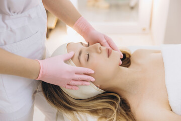 Cosmetic professional performing facial massage on relaxed blonde client following aesthetic procedure in medical spa setting