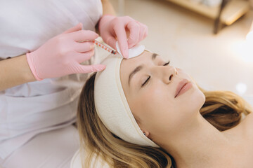 Fototapeta premium Cosmetologist making rejuvenating injection on forehead of young woman for reducing wrinkles in beauty salon