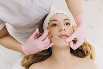 Cosmetologist injecting filler into female lips in cosmetology clinic, making botox injection for...