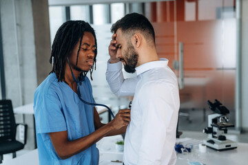 Doctor is using stethoscope, listening the heart of patient. Two men are in the office