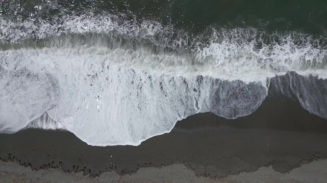 Wave foam. Waves breaking on the volcanic beach. Aerial overhead view with traveling shot. Coastline. Canary Islands. Spain.
