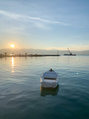 Serene sunset over calm water with a lone wooden boat floating near the shore.