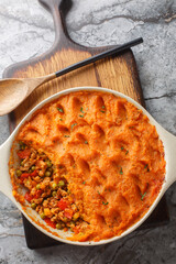 Homemade Sweet Potato Shepherd's Pie with mince and seasonal vegetables close-up in baking dish on wooden board. Vertical top view from above