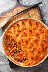 Healthy shepherd's pie made with ground meat, vegetables and topped with a layer of fluffy mashed sweet potatoes closeup on the baking dish on the wooden board. Vertical top view from above